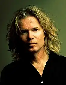 Adrian VanDenBerg wearing a black v-neck shirt, gazing intently at camera