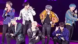 Seven men performing on stage against a purple background