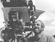 Black and white photograph; a man squints into the telescopic eyepiece of a large mechanical device.