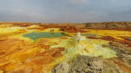 Image 16DallolPhotograph credit: Alexander SavinDallol is a cinder-cone volcano in the Danakil Depression, northeast of the Erta Ale Range in Ethiopia. The area lies up to 120 m (390 ft) below sea level, and has been repeatedly flooded in the past when waters from the Red Sea have inundated it. The Danakil Depression is one of the hottest places on Earth, and the evaporation of seawater after these flooding episodes produced thick deposits of salt, as seen in this landscape. The deposits at Dallol include significant quantities of the carbonate, sulfate and chloride salts of sodium, potassium, calcium and magnesium. Hot springs discharge brine to form the blueish ponds, and small, temporary geysers produce cones of salt.More selected pictures
