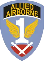 A blue shield with the word "Allied Airborne" on a black background near the top. The centre of the shield contains a white number one with yellow wings. At the bottom, a pair of crossed gladiator swords point down, on a purple-red background.