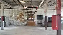 An open room with a wooden floor and a brick wall. The room's wooden ceiling is held up by wooden beams and wooden supports. A large sliding door is open, revealing similar rooms beyond.