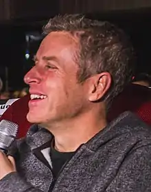 A man with brown hair smiling while facing to the left of the camera