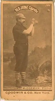 A baseball player is shown on his right profile, standing in his uniform.