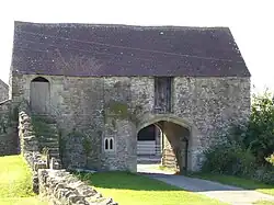 Stone building with archway through it for the road. Steps to wooden doorway on the first floor.