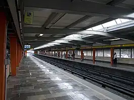 Multiple people wait at the long platforms of a station.