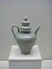 A green-tinted grey teapot with a small base and a tall body in the shape of a cone with the smallest point facing downwards. The cap covering the point that the water is poured into is a tall cylinder, and fits into a thick, wide cylindrical rim in the pot.