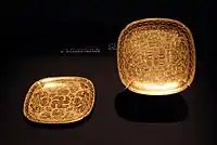 A pair of square lobed gold dishes with chased insects, flowers and knotted ribbons