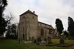 A stone church seen from the southwest, in the foreground a large, squat tower with a pyramidal roof, and the body of the church extending behind it