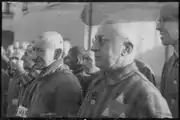 Sachsenhausen detainee with glasses in the foreground wears a two-color double-triangle ID-emblem.